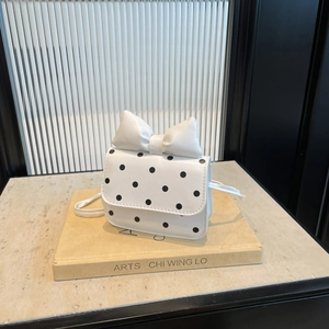 Polka dot mini shoulder bag with large bow decor on beige stone book display stand
