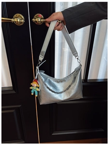 Close-up of silver metallic crescent shoulder bag with wide strap and cartoon doll charm
