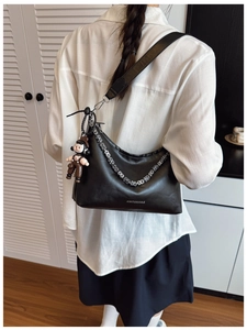 Detail of black crescent shoulder bag with metallic chain and cute cartoon charm