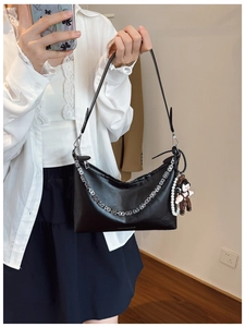 Detail of black hobo bag featuring bold silver chain and cute pearl doll charm accessory