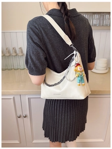 Detail of cream-colored hobo bag with logo, metal chain, and cute cartoon doll pendant