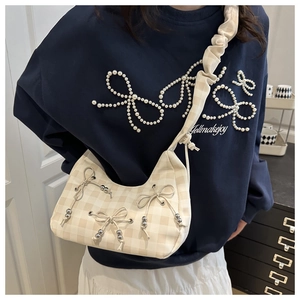 Dettaglio borsa a mezzaluna beige a scacchi con fiocchi decorativi e tracolla plissettata