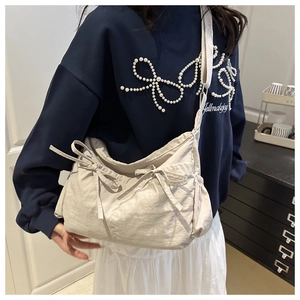 Dettaglio di una borsa a tracolla in nylon crema con fiocchi decorativi e stile casual