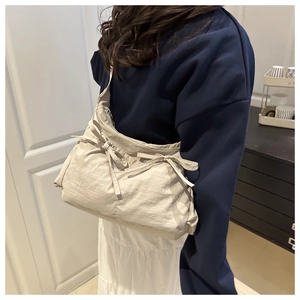 Detail view of cream crossbody bag featuring decorative bows and soft wrinkled fabric texture