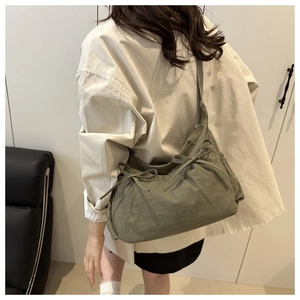 Side view of an olive green nylon pleated shoulder bag with decorative bow drawstrings