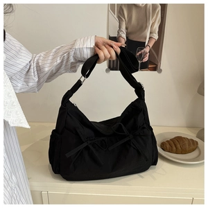 Detail of black nylon crossbody bag with bow accents and elastic side pockets