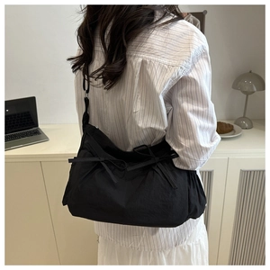 Close-up of black crossbody bag featuring elegant ribbon bows and pleated fabric details