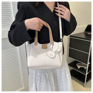 Detail of cream bucket bag with brown handles and a cute white rabbit pendant charm
