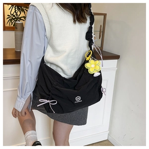 Détail du sac bandoulière plissé noir avec ruban rose et breloque fleur jaune