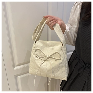 Dettaglio di una borsa a tracolla beige plissettata con un fiocco sottile e patta sopra