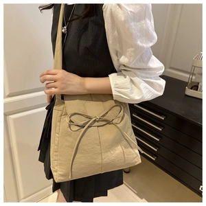 Dettaglio della borsa a tracolla in tela beige con grande fiocco decorativo frontale