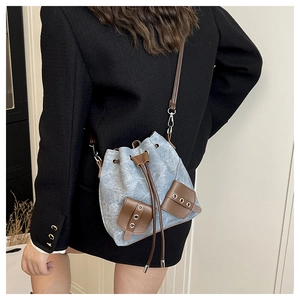 Detail of blue denim bucket bag with brown leather contrast stitching and drawstring closure