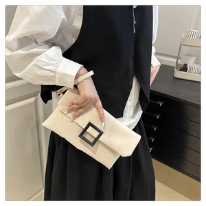 Detail of a creamy beige envelope clutch with a large black square buckle and matte texture