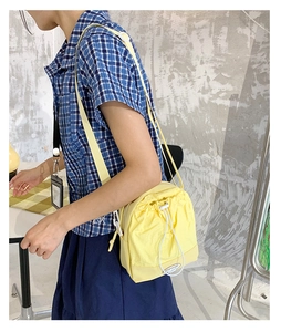 Close-up of yellow nylon crossbody bag with drawstring closure and fashion logo on model