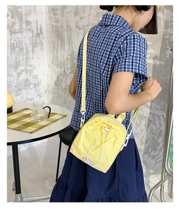 Detail of yellow nylon drawstring crossbody bag featuring side clips and fashion logo