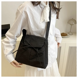 Dettaglio della borsa a tracolla in nylon nero con un delicato fiocco sulla patta