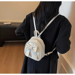 Detail shot of a mini cream bow backpack worn on back, showcasing chic compact design