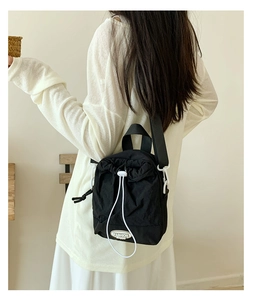 Detail of black nylon drawstring crossbody bag with Fashion Happy label on white outfit