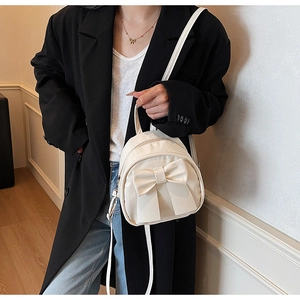 Detail of a chic cream-white backpack with a large decorative bow on a black blazer