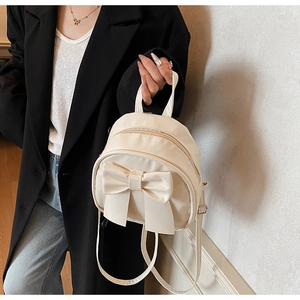 Detail of mini cream faux leather backpack featuring a large decorative bow and metal buckle