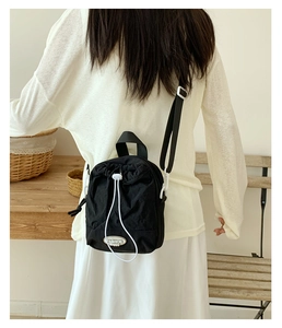 Detail of black nylon crossbody bag with drawstring closure and white cord accents