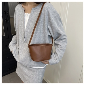Brown lychee leather bucket bag with FASHION embossed detail worn by a model