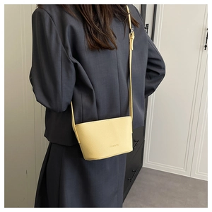 Detail of a bright yellow litchi-textured bucket bag worn by a model in a gray suit