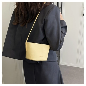 Detail of yellow litchi pattern bucket bag on female model in grey suit attire