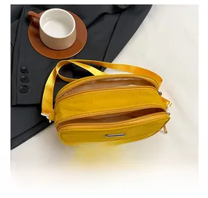 Detail view of bright yellow nylon crossbody bag with three zipper compartments and strap