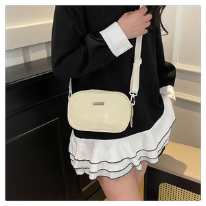 Close-up of a cream shell-shaped crossbody bag featuring metal logo and fabric strap