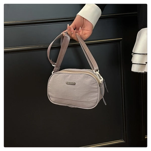 Detail of grey-purple nylon crossbody bag with dual zippers and metal brand plaque