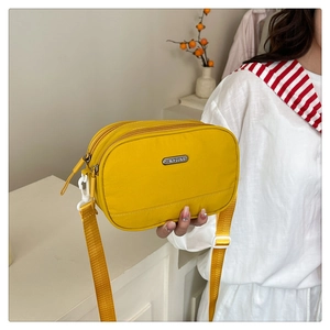 Detail of a yellow nylon crossbody bag featuring multi-layer zippers and metallic logo