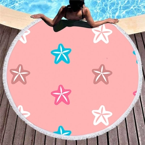 Round pink beach towel with blue starfish print and white tassels on a poolside wooden deck