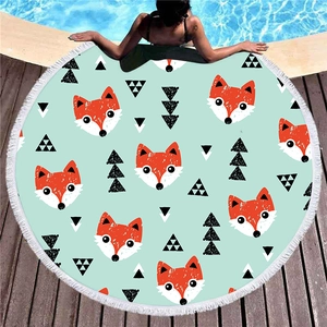 Round beach towel with orange fox patterns and white tassels on a poolside deck
