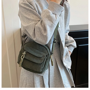 Close-up of dark green corduroy crossbody bag featuring a flap and woven zipper pullers