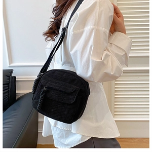 Side view of a black corduroy crossbody square bag featuring a unique woven zipper pull
