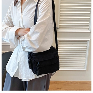 Detail of black corduroy crossbody bag with woven zipper pull and front flap pocket