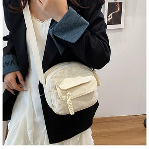 Detail of cream white corduroy crossbody bag with woven zipper pull on a model