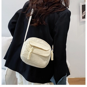 Detail of a creamy beige corduroy crossbody bag with a woven rope zipper and outer flap pocket