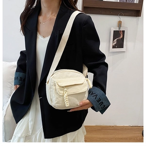 Detailed view of beige corduroy crossbody bag with woven zipper and wide fabric strap