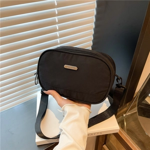 Minimalist black nylon crossbody bag with adjustable strap and metal logo plaque