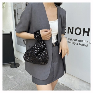 Close-up of a sparkling black sequin wrist bag with a twisted handle design on a grey suit