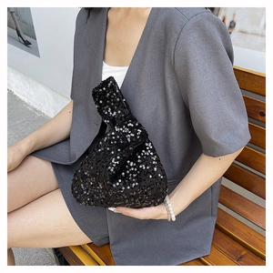 Close-up of a black sequin wrist bag with a unique knot handle on a gray suit outfit