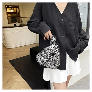 Detail of elegant black sequined wrist bag featuring shiny silver texture and knotted handle