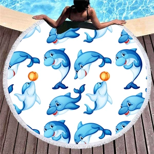 Round beach towel with blue dolphin patterns and white tassel fringe on a pool deck
