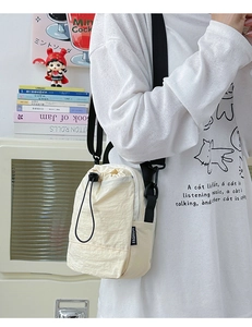 Detail of a creamy white nylon crossbody bag featuring a drawstring closure and black strap
