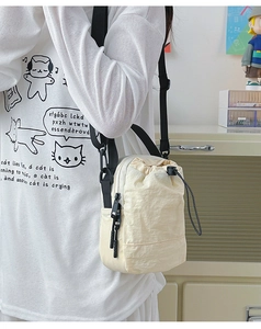 Detail of lightweight cream nylon crossbody bag with drawstring closure and side zipper