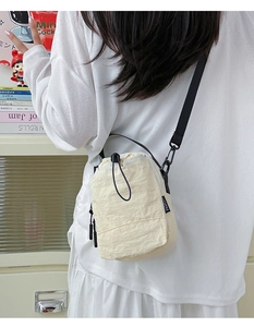 Detail of beige drawstring crossbody bag with textured fabric and fashion logo tag