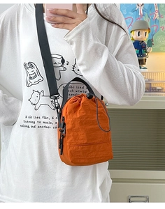 Detail of orange lightweight nylon crossbody bag with drawstring closure and adjustable strap
