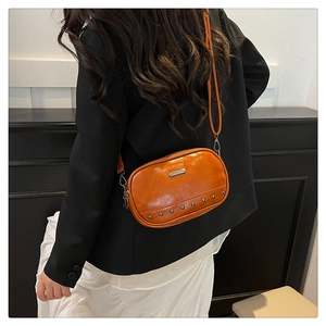 Detail view of orange crossbody bag with metal rivets and rectangular logo on fine leather